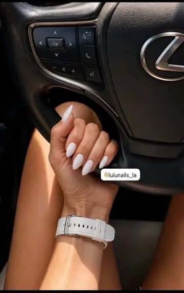 White almond nails resting on a car steering wheel